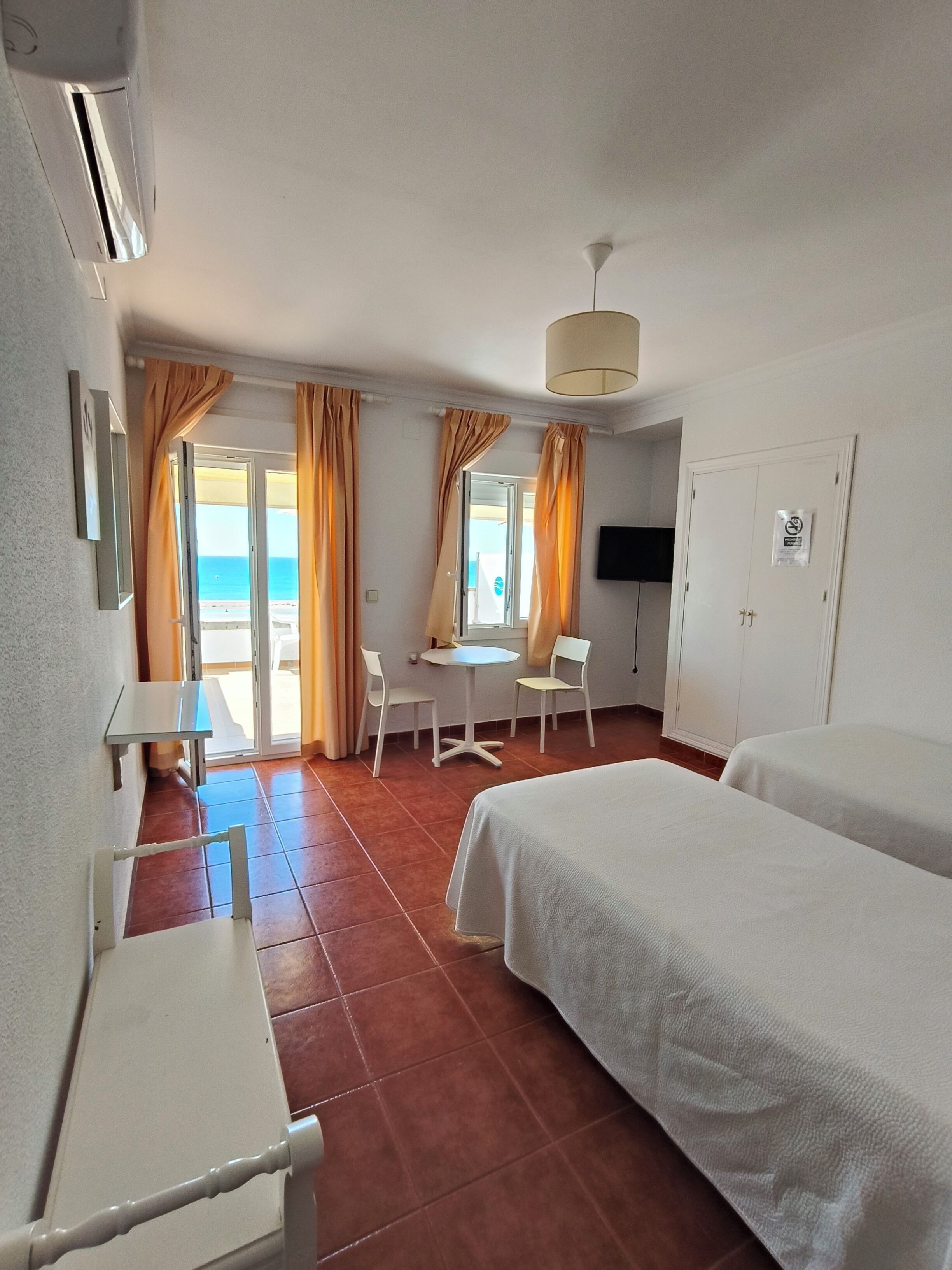 A hotel room with a bed, a desk, a chair, a small table, and a television.