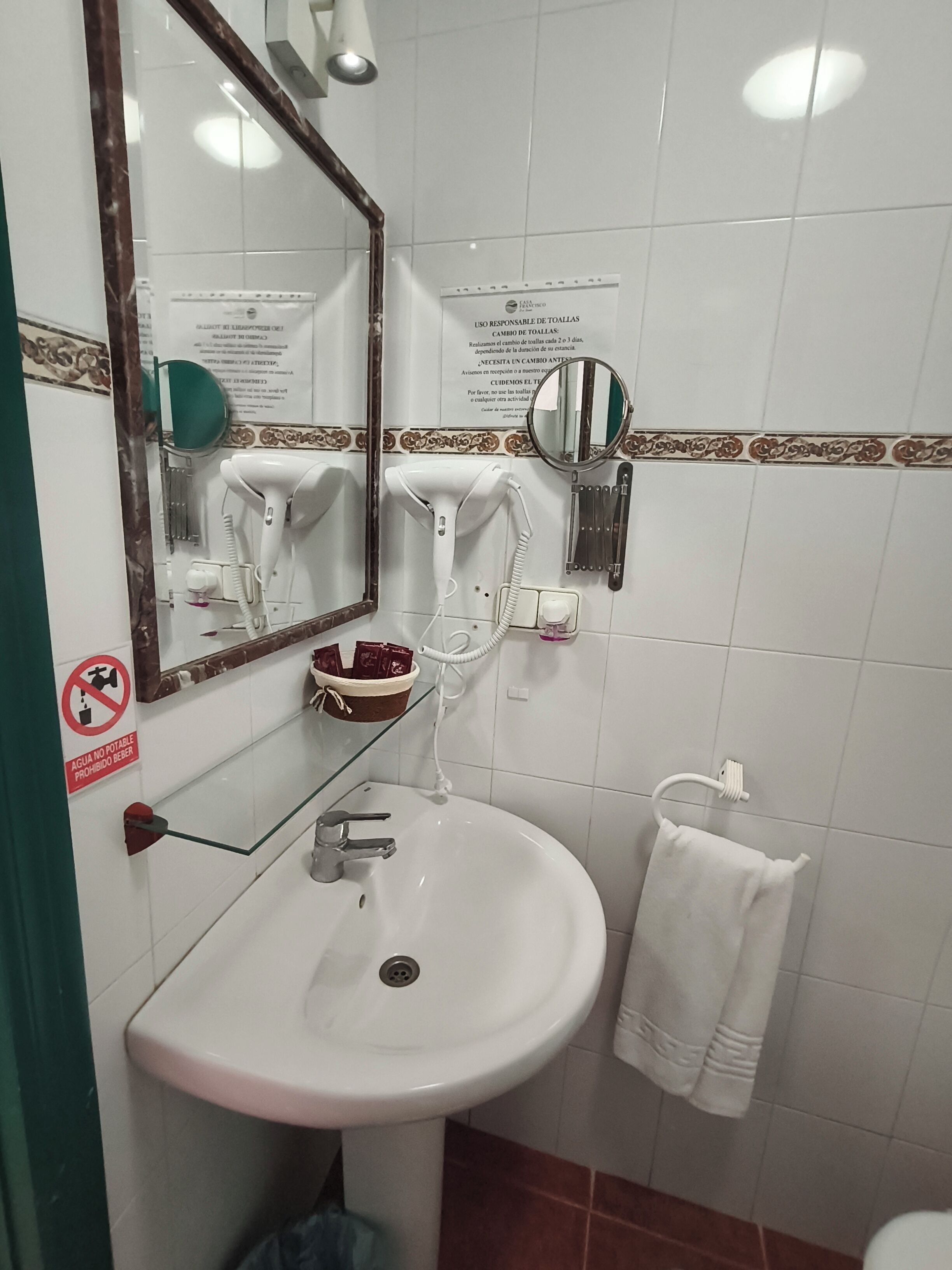 A bathroom with a sink, mirror, towel rack, and a no-drinking sign.