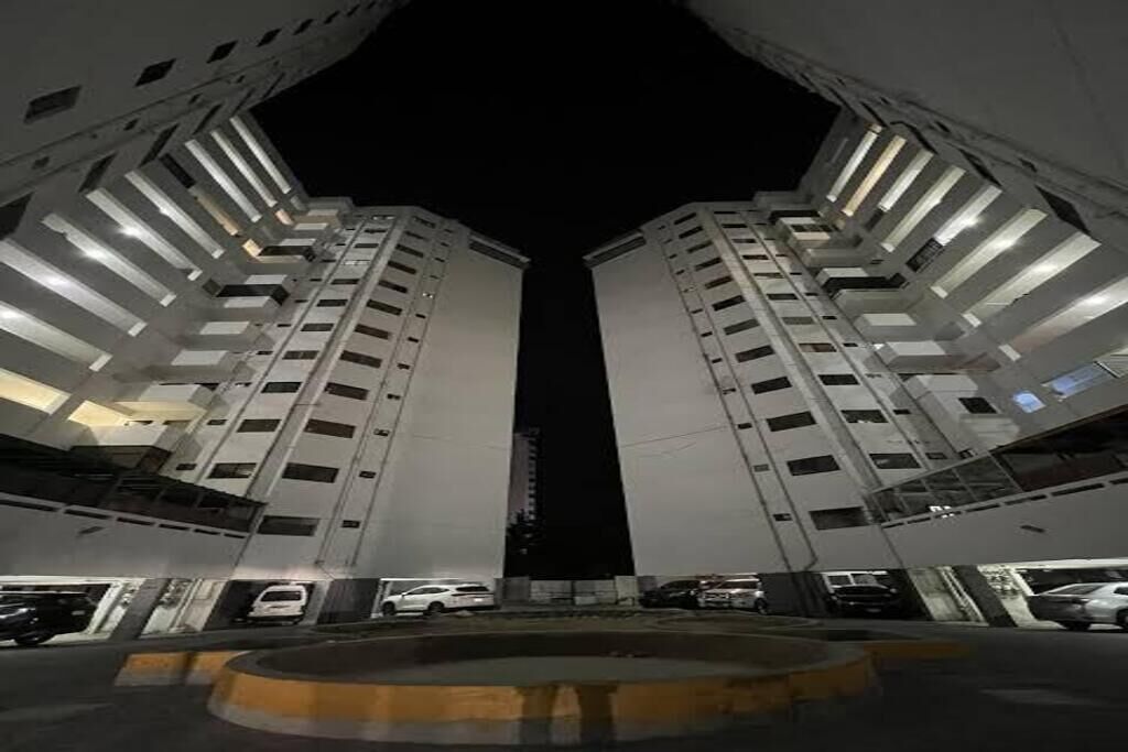 Vista nocturna de un edificio moderno con dos torres simétricas, un espacio central vacío y un camino de acceso circular.