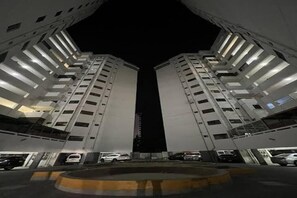 Vista nocturna de un edificio moderno con dos torres simétricas, un espacio central vacío y un camino de acceso circular.