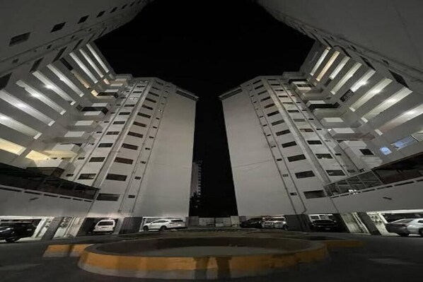 Vista nocturna de un edificio moderno con dos torres simétricas, un espacio central vacío y un camino de acceso circular.