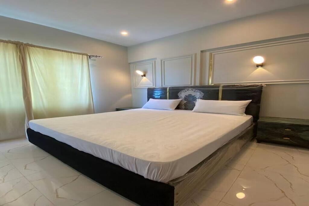 A hotel room with a large bed, two bedside lamps, and a window with curtains.