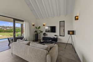 A living room with a sofa, a TV, and a floor lamp. - Villa Zaya Blue Bay Private Pool Golf View (Sint Michiel)
