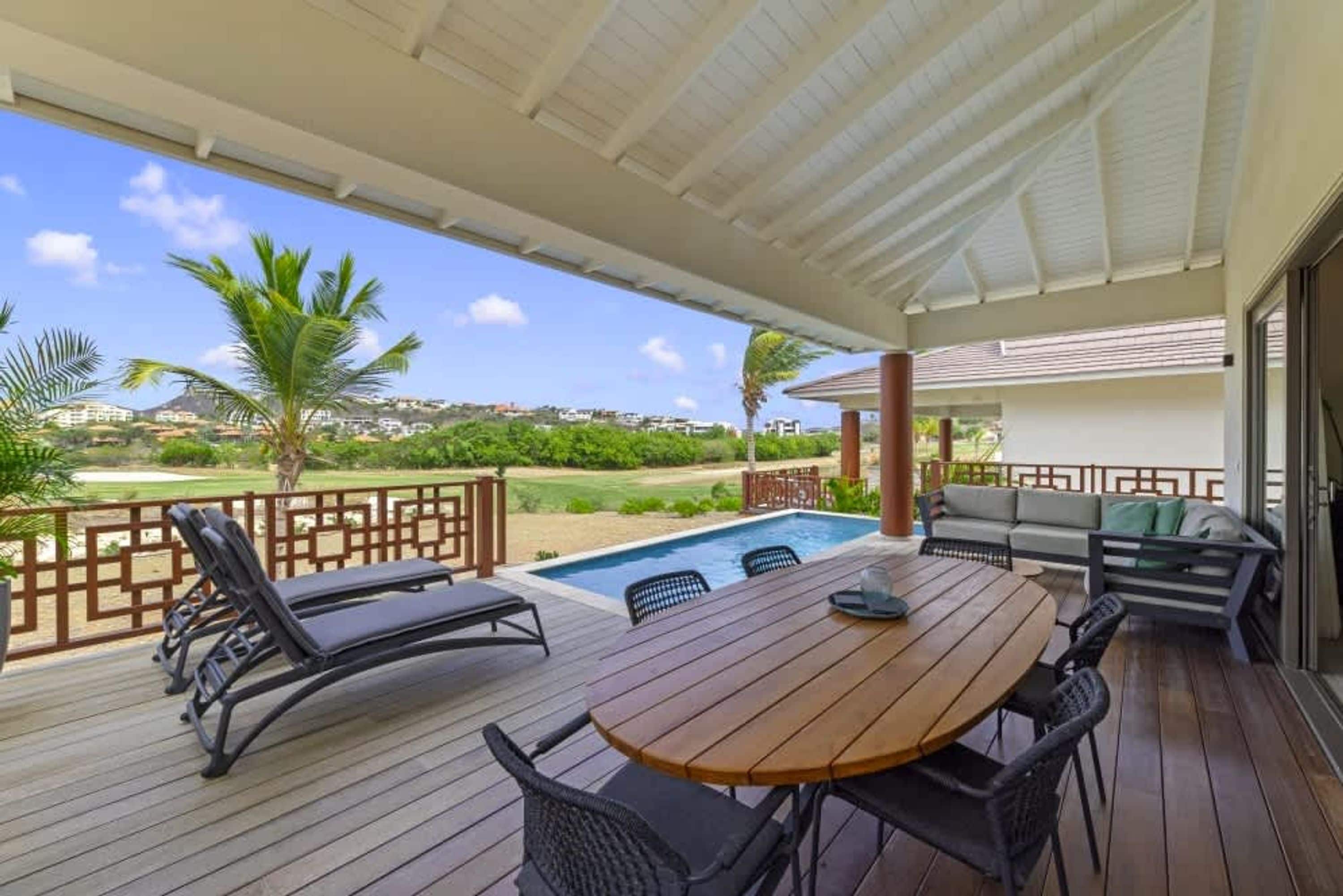 A covered outdoor area with a pool, lounge chairs, and a table.