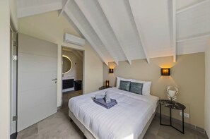 A bedroom with a bed, bedside lamps, a small table, and a door leading to another room. - Villa Zaya Blue Bay Private Pool Golf View (Sint Michiel)