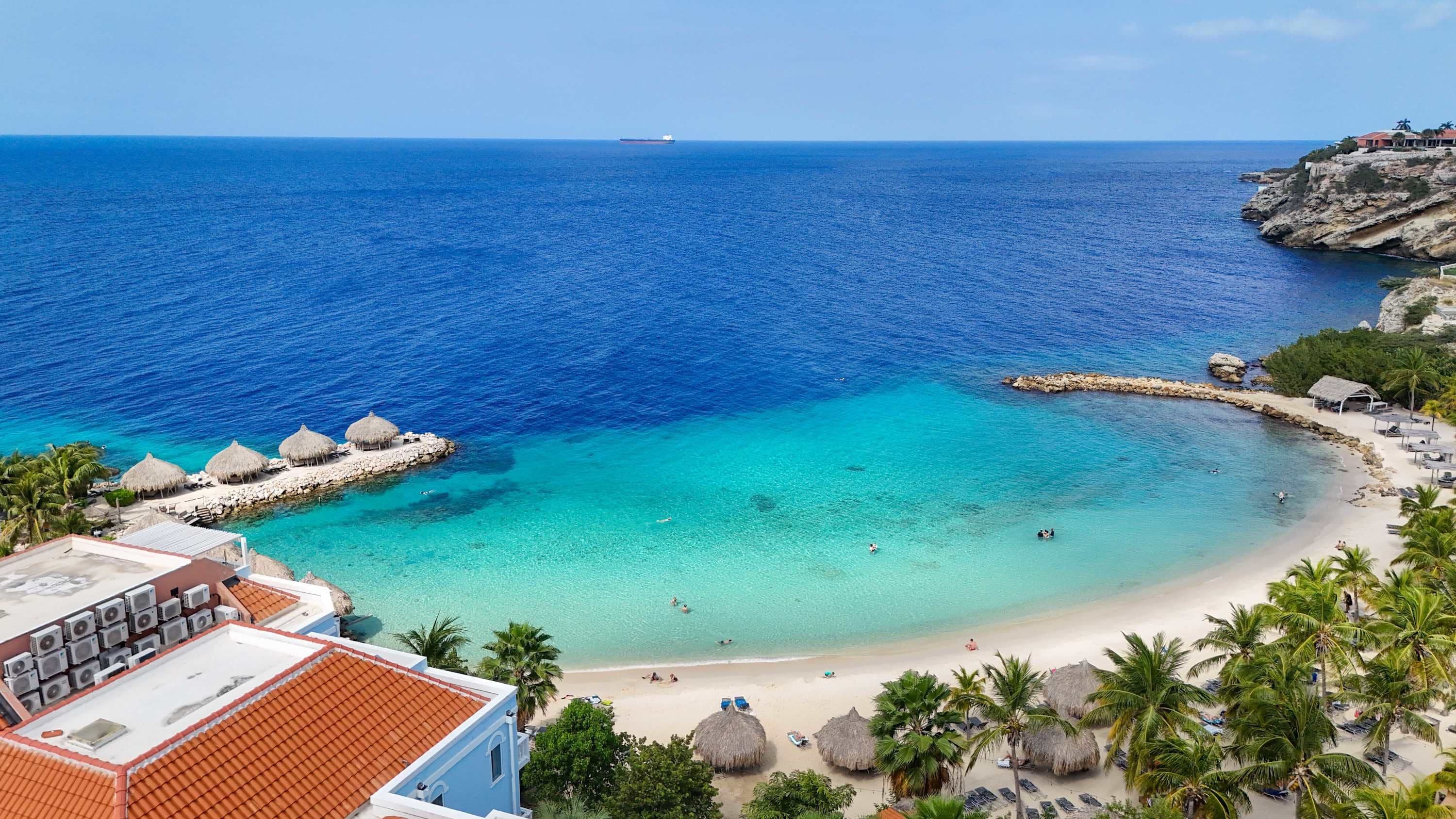 Una vista costiera con un mare blu limpido, una spiaggia sabbiosa e una scogliera rocciosa.