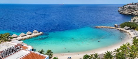 A coastal view with a clear blue sea, a sandy beach, and a rocky outcrop.