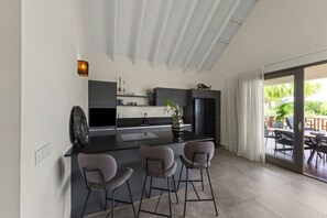 A modern kitchen with a central island, bar stools, and a view of the outdoor patio. - Villa Zaya Blue Bay Private Pool Golf View (Sint Michiel)