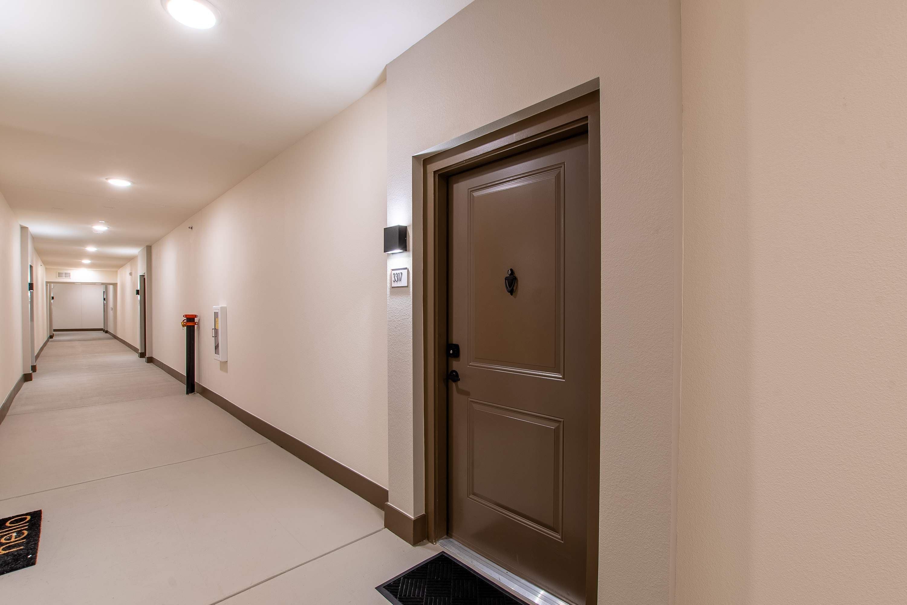 Pasillo de hotel con una puerta marrón, un detector de incendios y un cartel con un número.