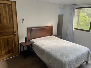 Ein Einzelbett mit Holz-Kopfteil, ein Nachttisch und ein Fenster mit Vorhängen.