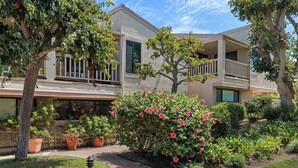 A two-story residential building with a covered balcony, a well-maintained garden with flowering bushes, and a brick pathway leading to the entrance. - Starfish Siesta - new listing! renovated condo with tennis, pool and patio (Solana Beach)
