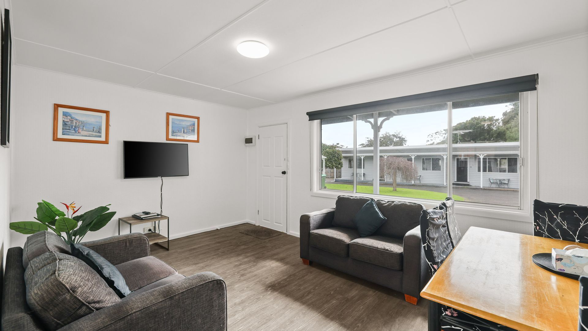 A modern living room with a grey sofa, a television, and a window with a view of a residential area.