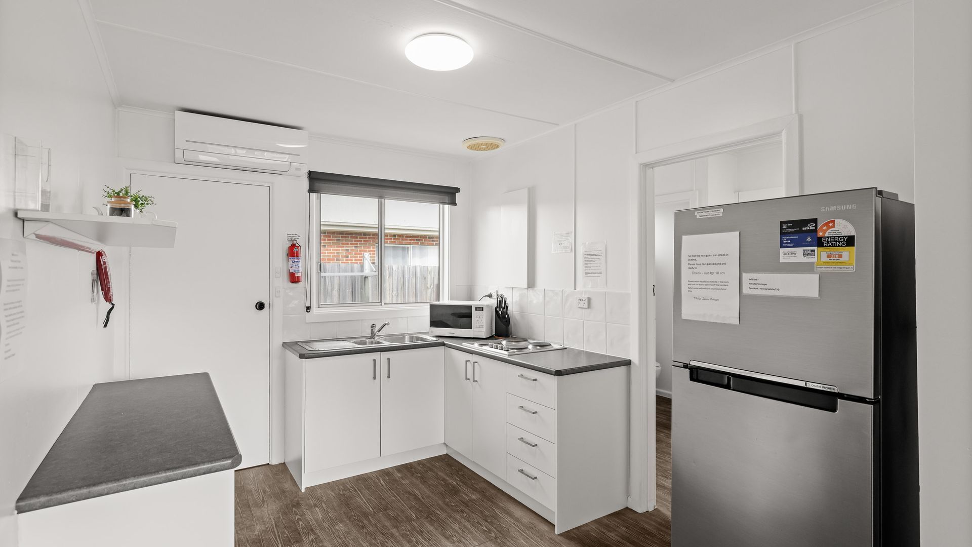 Una cocina moderna con armarios blancos, un refrigerador de acero inoxidable, un microondas y un lavamanos.