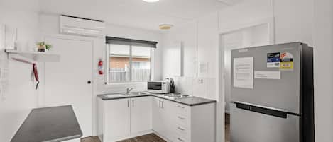 A modern kitchen with white cabinetry, a stainless steel refrigerator, a microwave, and a sink.