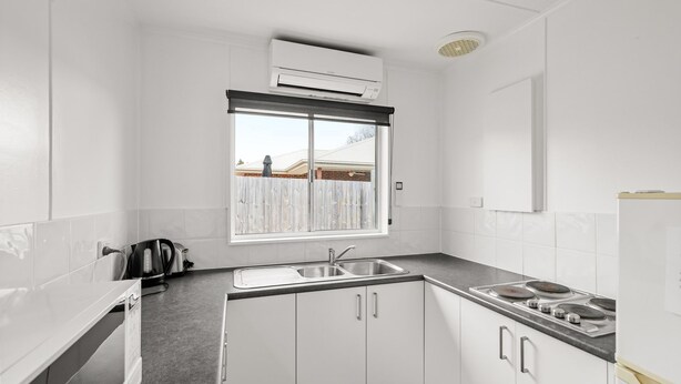 A kitchen with white cabinets, a double sink, a stove, and a window with a view of a fence and a building.