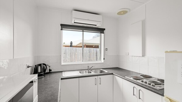 A kitchen with white cabinets, a double sink, a stove, and a window with a view of a fence and a building.