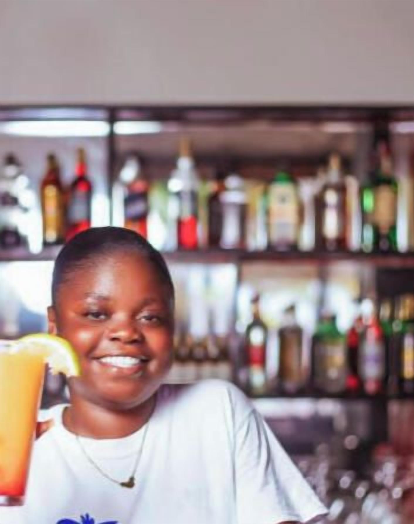 A person holding a drink at a bar with a background of various bottles.