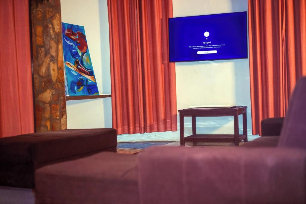 A room with a television displaying a 'No Signal' message, a painting on the wall, and a red curtain.