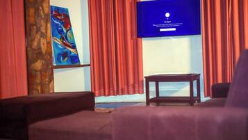 A room with a television displaying a 'No Signal' message, a painting on the wall, and a red curtain.