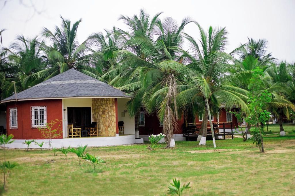 A bungalow with a tiled roof, surrounded by palm trees and a grassy lawn.