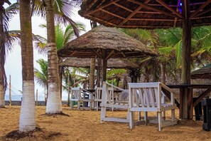 Una playa con sombrillas de paja y sillas de madera.