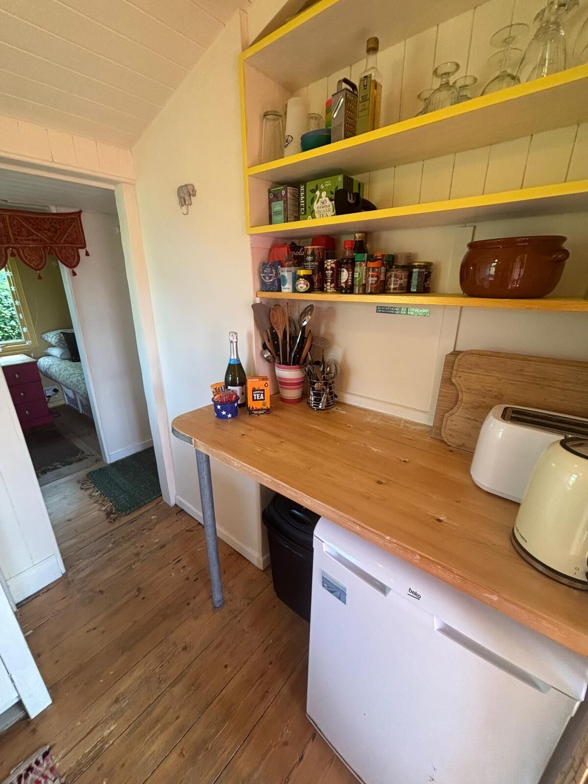 A compact kitchen with wooden countertops, a white refrigerator, and a yellow shelf with various kitchen items.