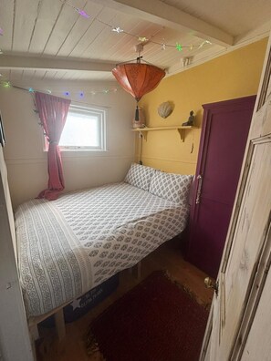 Ein Schlafzimmer mit einem Bett, einem Fenster mit Vorhängen, einer Ablage mit Dekoration und einem lila Kleiderschrank.