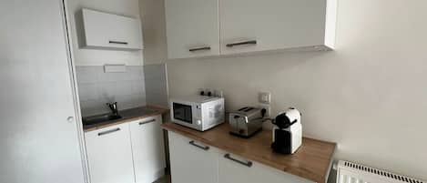 Cozinha com armários brancos, micro-ondas, torradeira e chaleira sobre o balcão.
