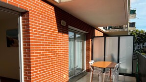 Un balcon avec un mur en briques, une porte-fenêtre coulissante, une table avec des chaises et une vue sur un bâtiment en arrière-plan.