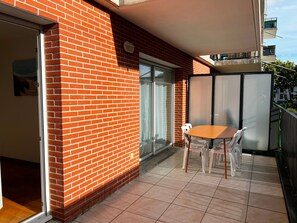 A balcony with a brick wall, a sliding glass door, a table with chairs, and a view of a building in the background. - Cosy apartment in city centre - 4 guests (La Teste-de-Buch)