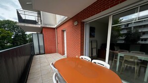 Un balcon avec une table et des chaises, une porte-fenêtre coulissante et un mur en briques rouges.