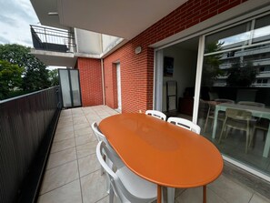 A balcony with a table and chairs, a sliding glass door, and a red brick wall. - Cosy apartment in city centre - 4 guests (La Teste-de-Buch)