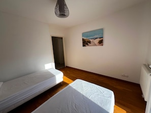A room with two single beds, a wooden floor, a painting on the wall, and a door leading to another room. - Cosy apartment in city centre - 4 guests (La Teste-de-Buch)