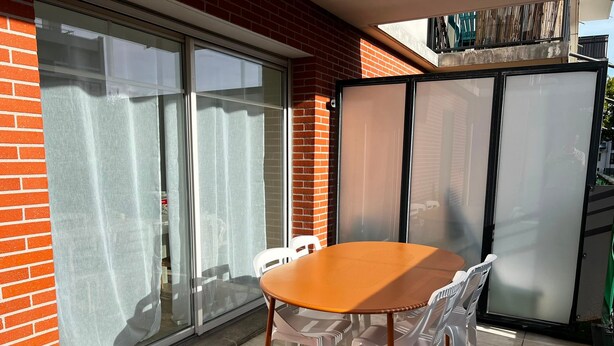 Une terrasse avec une table ronde et des chaises, une porte-fenêtre coulissante et un mur en briques.