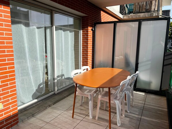 A patio with a round table and chairs, a sliding glass door, and a brick wall. - Cosy apartment in city centre - 4 guests (La Teste-de-Buch)
