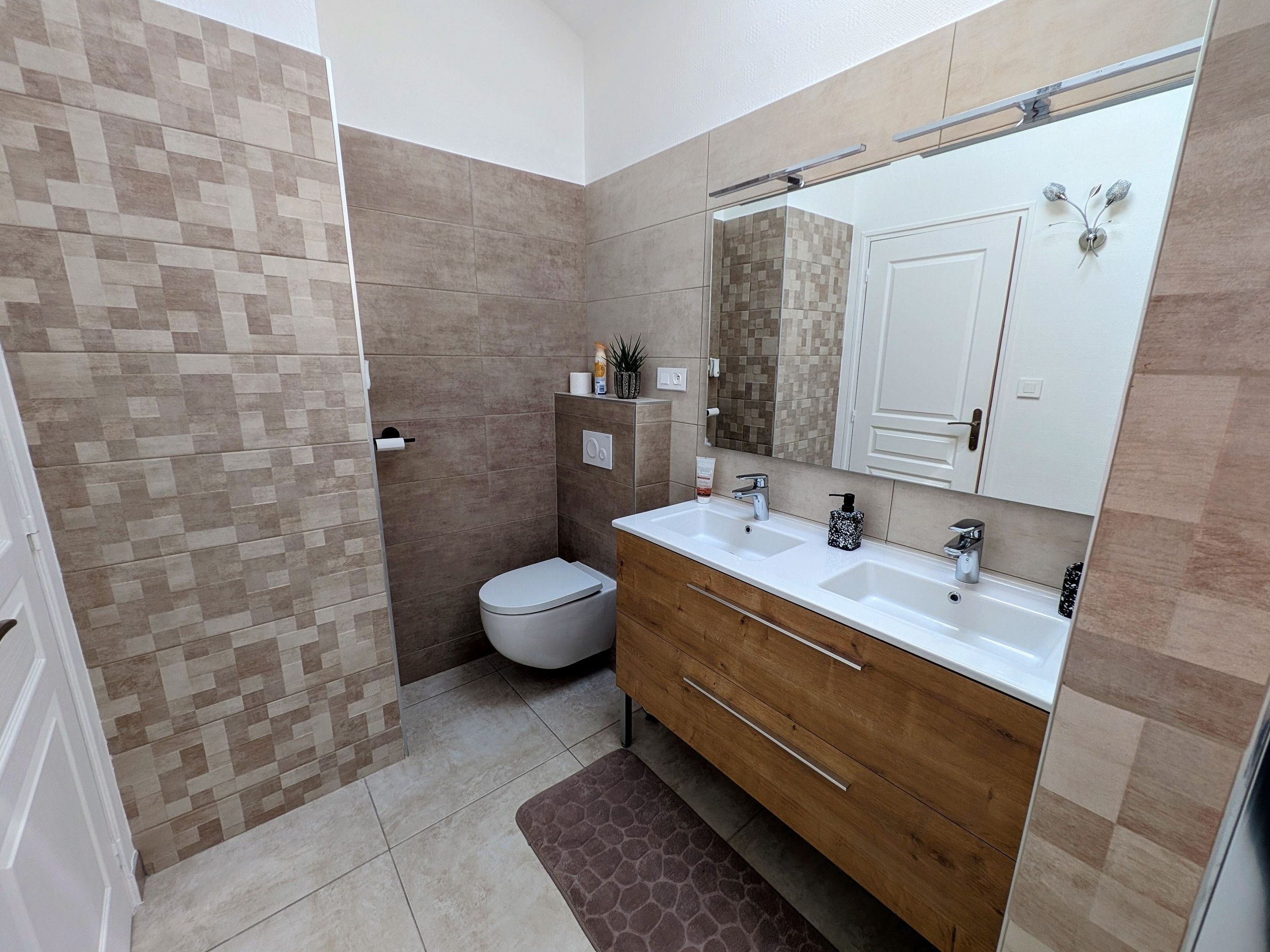 Une salle de bain moderne équipée d’une douche, de toilettes et de deux lavabos.