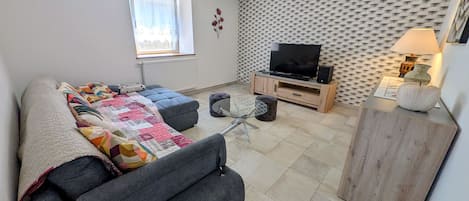 A modern living room with a sofa, ottoman, TV stand, and a lamp.