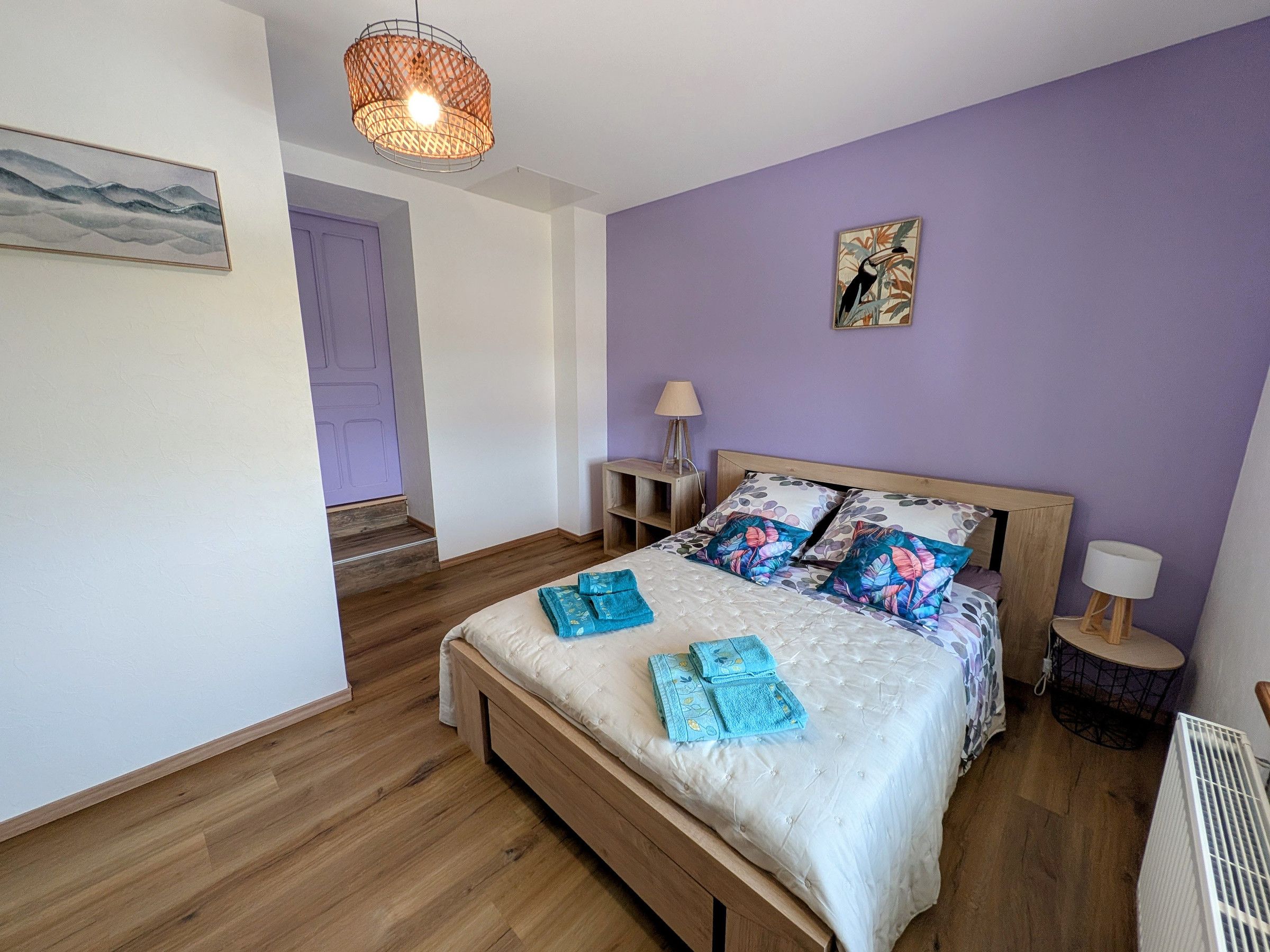 A bedroom with a wooden bed, a nightstand, a lamp, and a wall art piece.