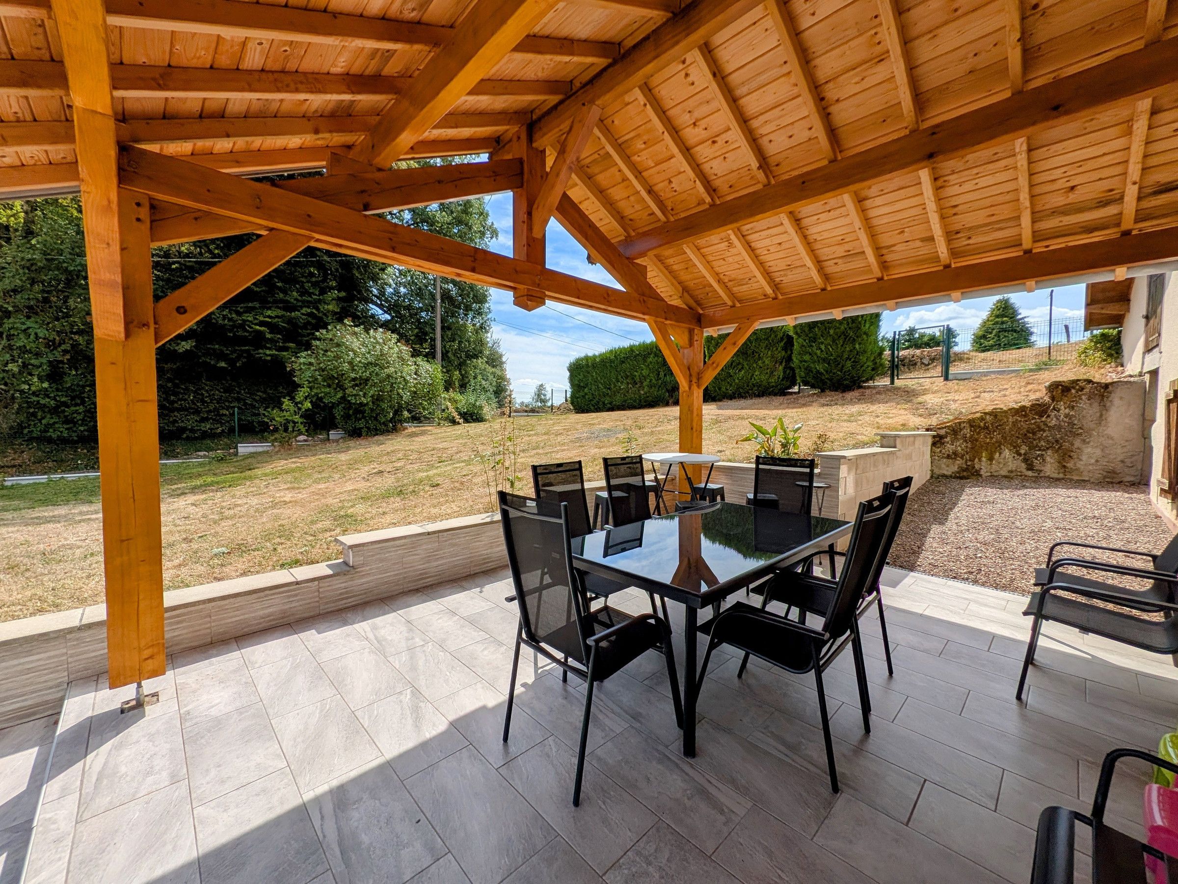 An outdoor patio with a wooden pergola, a glass-top table, and black chairs.