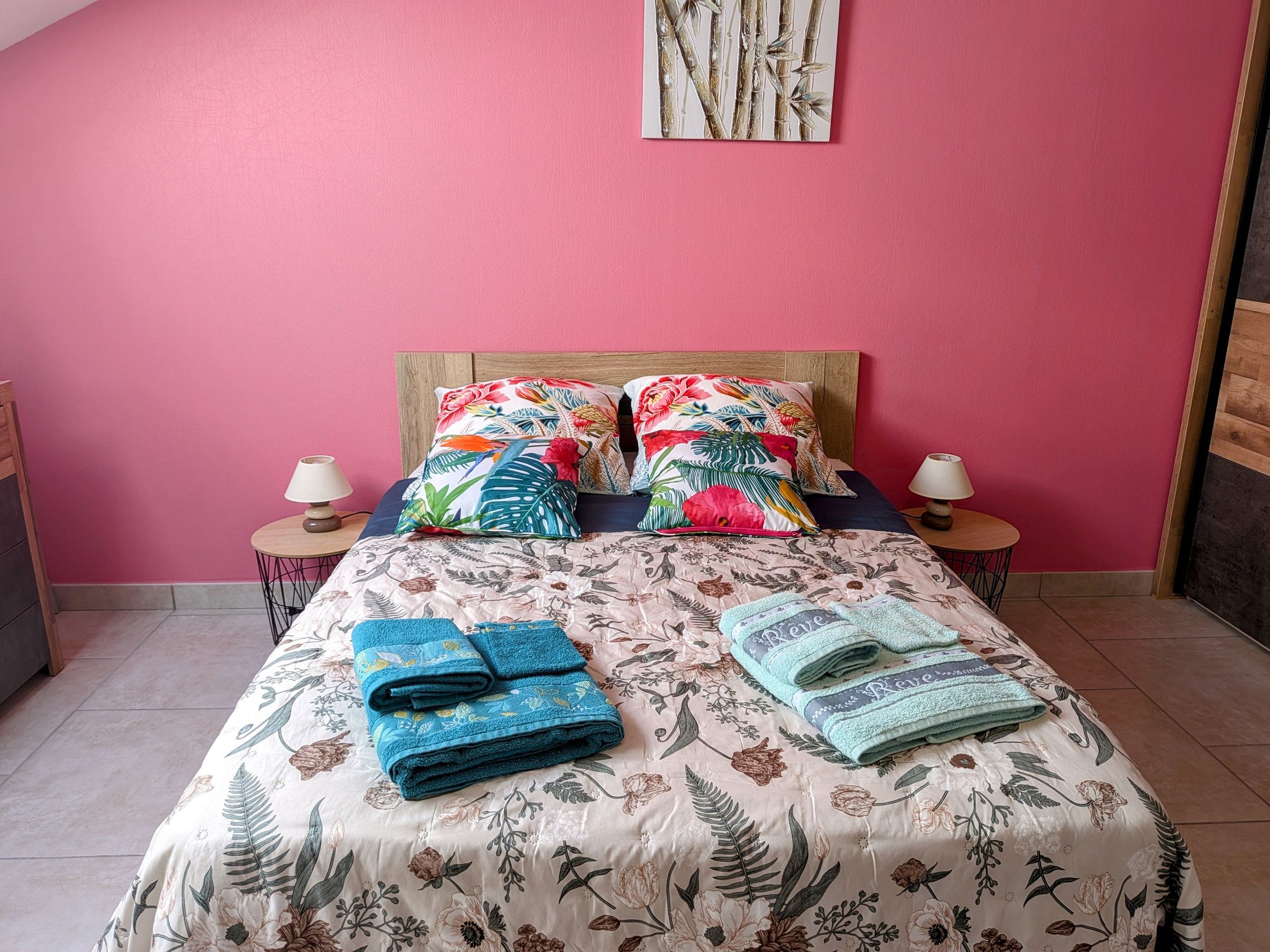 Un lit avec une literie à motifs floraux, deux oreillers, deux tables de chevet avec des lampes et des serviettes pliées.