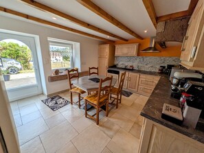 A kitchen with wooden cabinets, a dining table with chairs, and a view through the door. - Spacious house in the heart of nature - 6 guests (Écromagny)