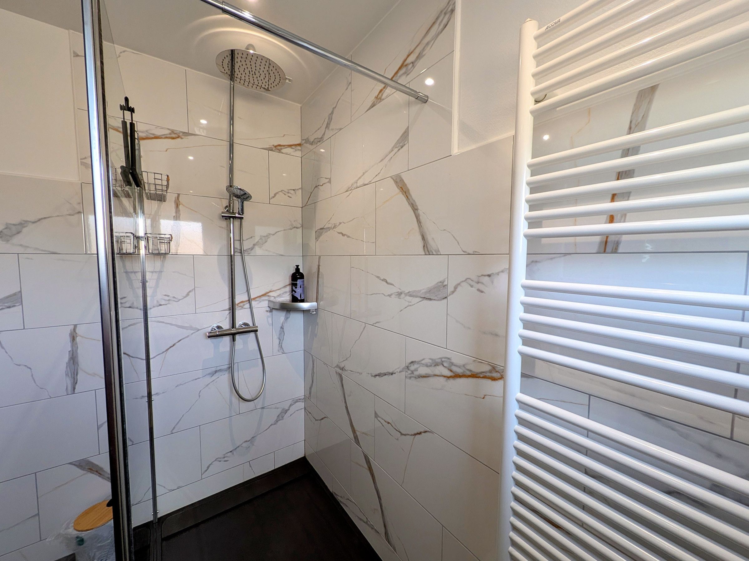 Une salle de bain moderne dotée d’une douche à parois de verre, de carreaux de marbre et d’un porte-serviettes intégré.