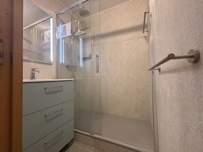 A bathroom with a glass shower enclosure, a vanity with a mirror, and a door with a towel rack. - Bright studio with terrace - 4 guests (La Plagne Montchavin Les Coches)