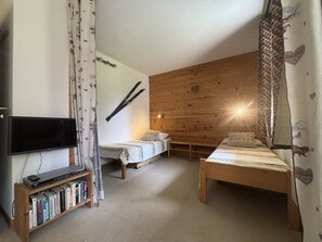 A room with two beds, a TV, and a bookshelf. - Bright studio with terrace - 4 guests (La Plagne Montchavin Les Coches)