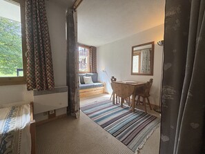 A cozy room with a window, a sofa, a small table, and a mirror. - Bright studio with terrace - 4 guests (La Plagne Montchavin Les Coches)