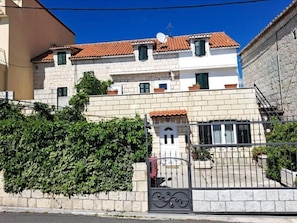 A two-story building with a tiled roof, a gated entrance, and a stone wall with greenery. - MARIO-50m from the beach,big terrace with sea view. FREE PARKING (Stobreč)