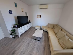 A living room with a sofa, a coffee table, a TV on a stand, a small plant, and a white cabinet. - MARIO-50m from the beach,big terrace with sea view. FREE PARKING (Stobreč)