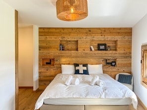 Ein Schlafzimmer mit einem hölzernen Kopfende, einem Bett mit weißer Bettwäsche und einer Pendelleuchte.