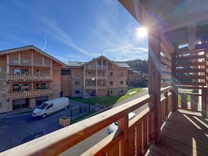 A wooden balcony with a view of a residential area, including a white van and a building with multiple balconies.