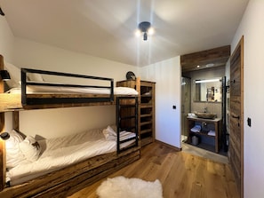 A compact room with two bunk beds, a wooden wardrobe, a small white rug, and a bathroom with a mirror and sink.